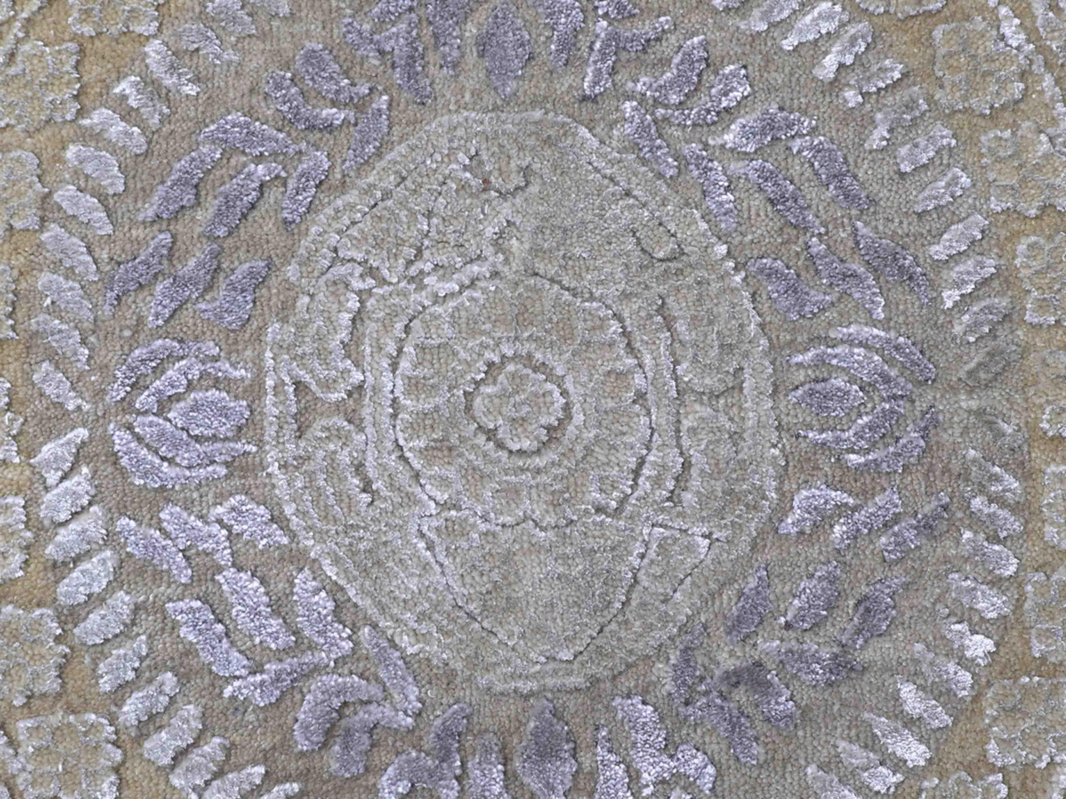 Close-up of a light gray and beige textured rug featuring an intricate circular pattern with floral and symmetrical designs, conveying elegance.