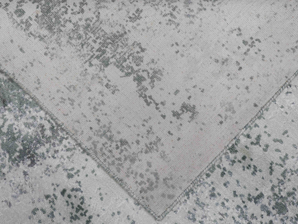 Close-up of a light grey, textured carpet with scattered dark grey abstract patterns, folded at one corner. The design conveys a modern, artistic feel.