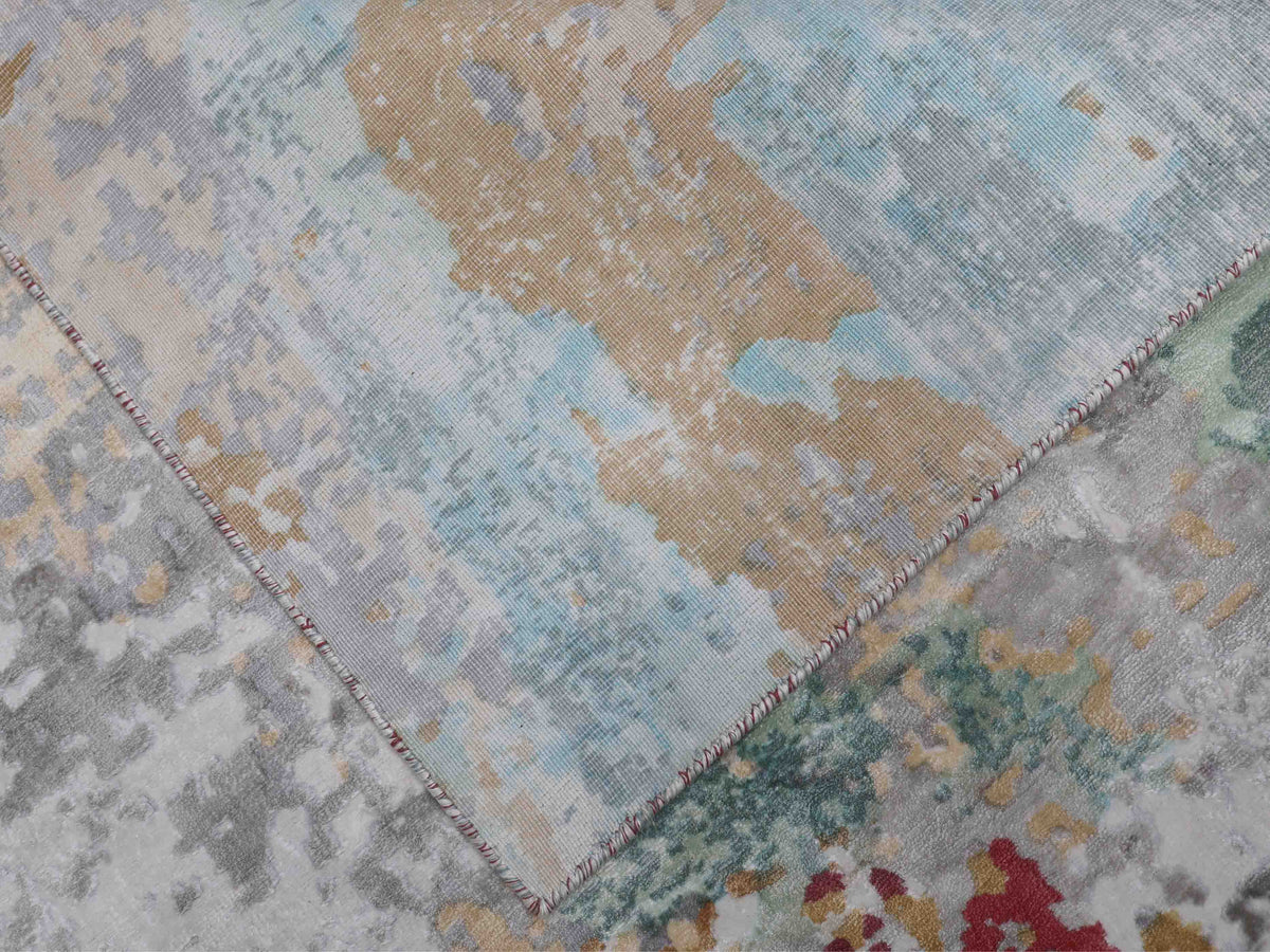 Close-up of an abstract-patterned rug with overlapping corners, featuring earthy tones like beige, light blue, red, and green, creating a textured, artistic feel.