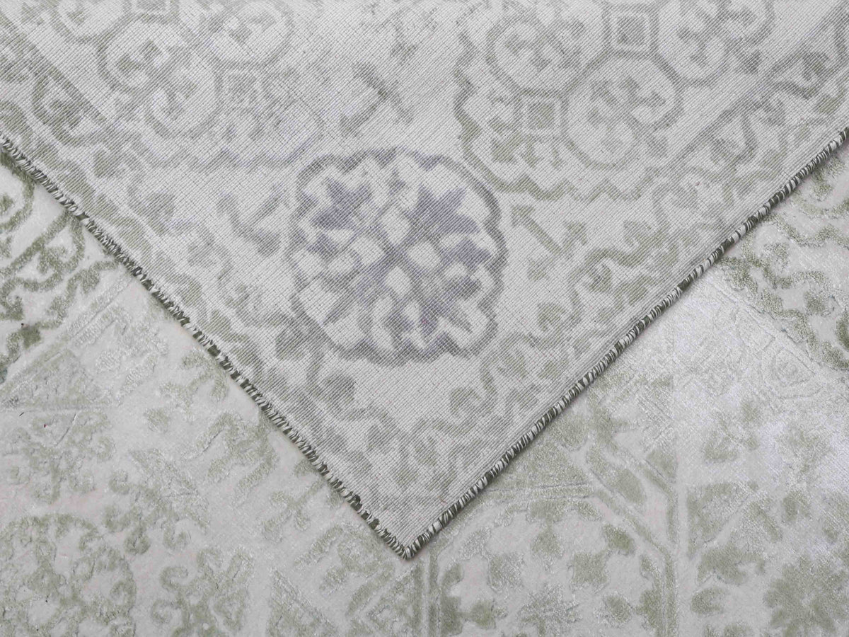 A close-up of a light-colored, patterned rug with a corner folded over, revealing intricate floral and geometric designs. Elegant and textured.