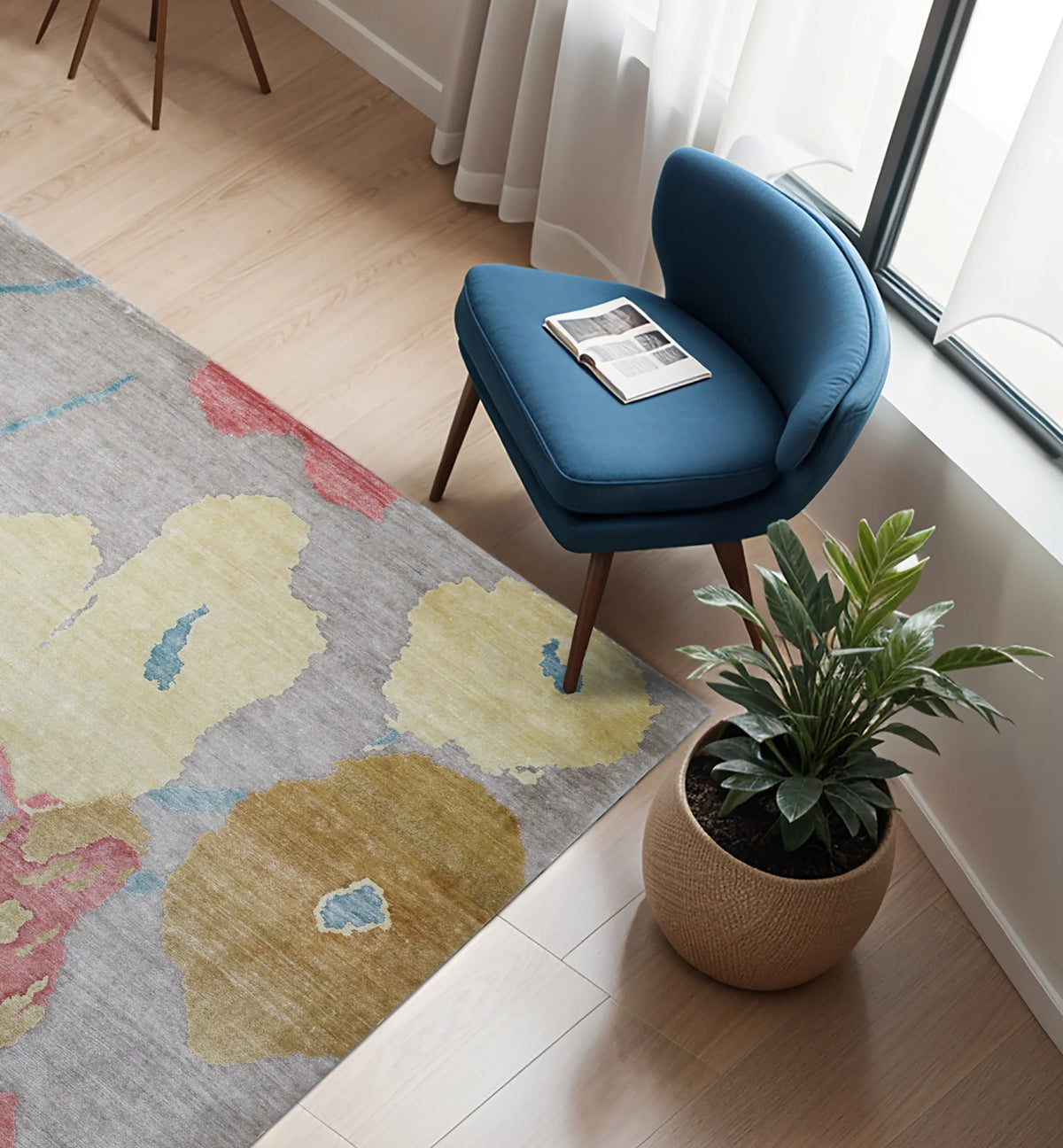 Handmade abstract floral area rug in grey, yellow and red tones next to a blue velvet chair.