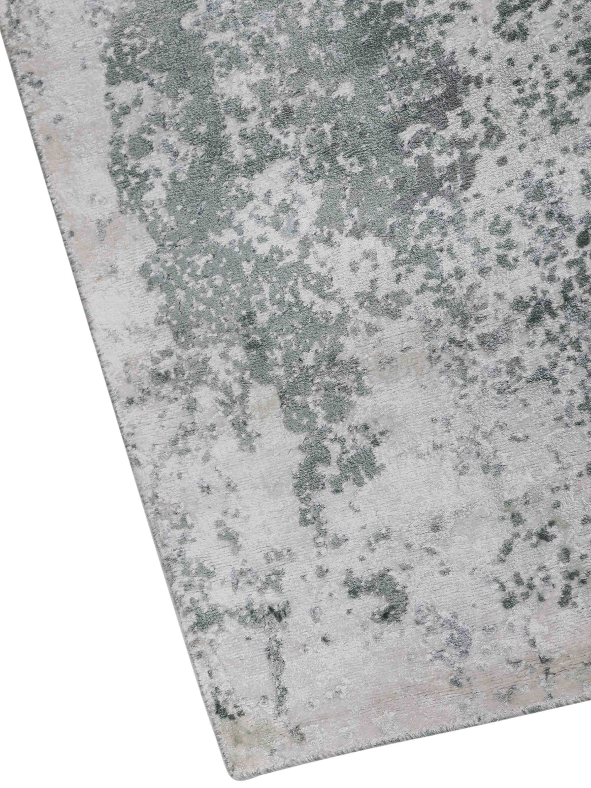 Close-up of a textured carpet with an abstract pattern. It features scattered green and gray blotches on a light background, evoking a natural, organic feel.