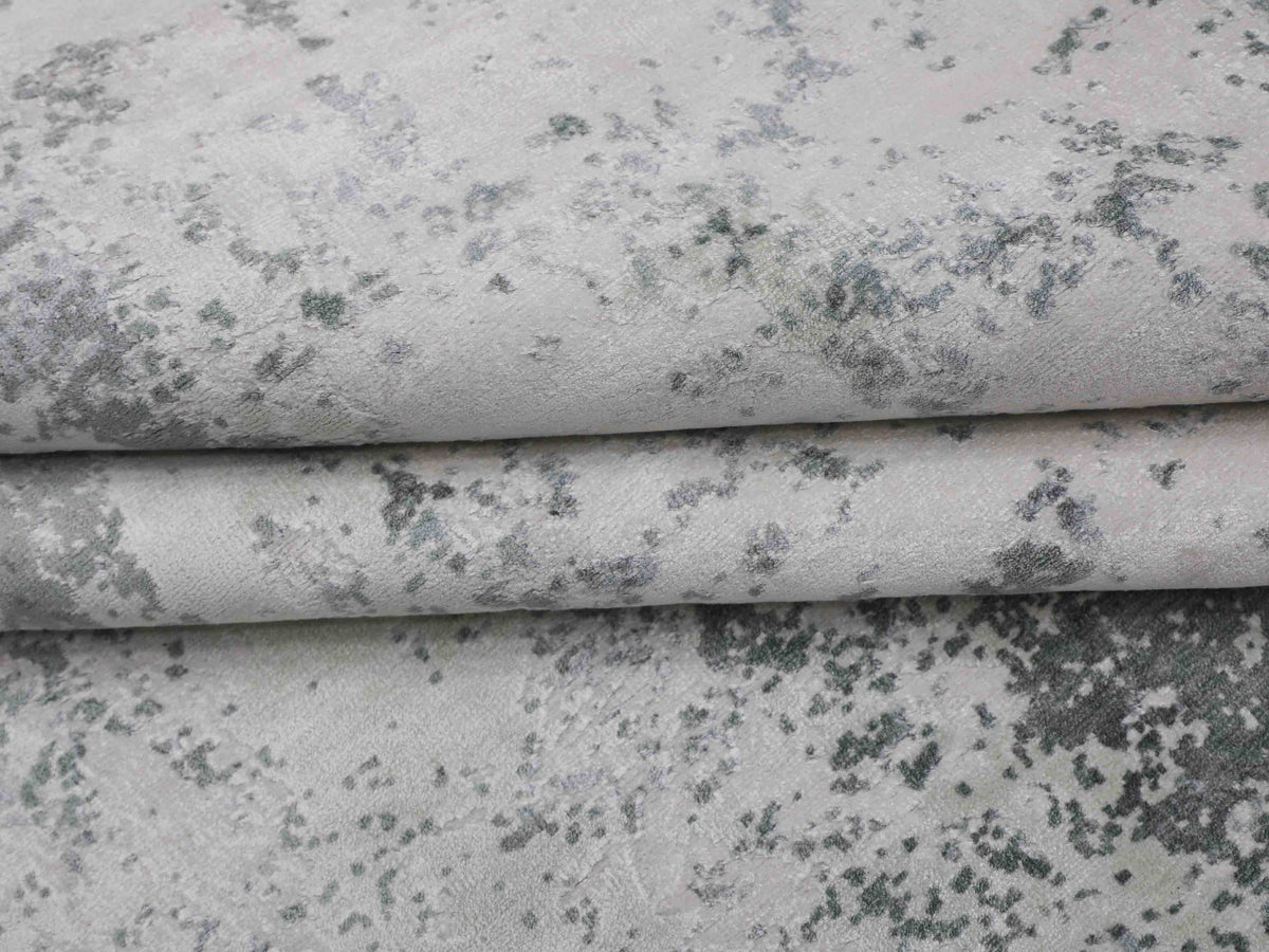 Close-up of a folded, grey and black speckled fabric with a textured, abstract pattern. The material appears soft and slightly plush.