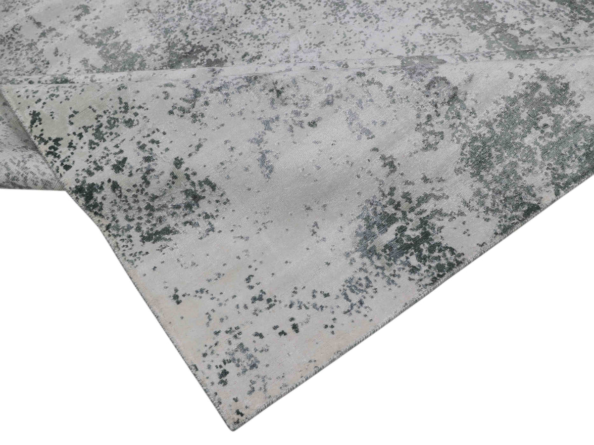 Folded, textured fabric with a mottled pattern of gray and white tones. The appearance is rough, resembling an abstract or weathered surface.