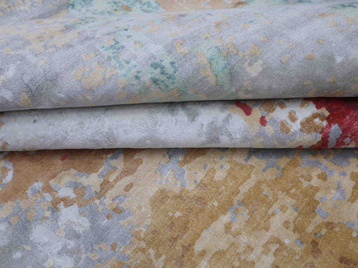 Textured fabric with a watercolor-like pattern in soft shades of beige, gray, green, and red. The folded layers create a serene, abstract impression.