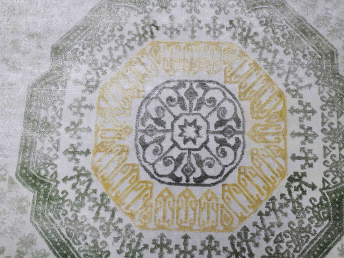 Ornate circular pattern featuring a central gray motif with swirling designs surrounded by a yellow band. Outer border is green with intricate detailing.