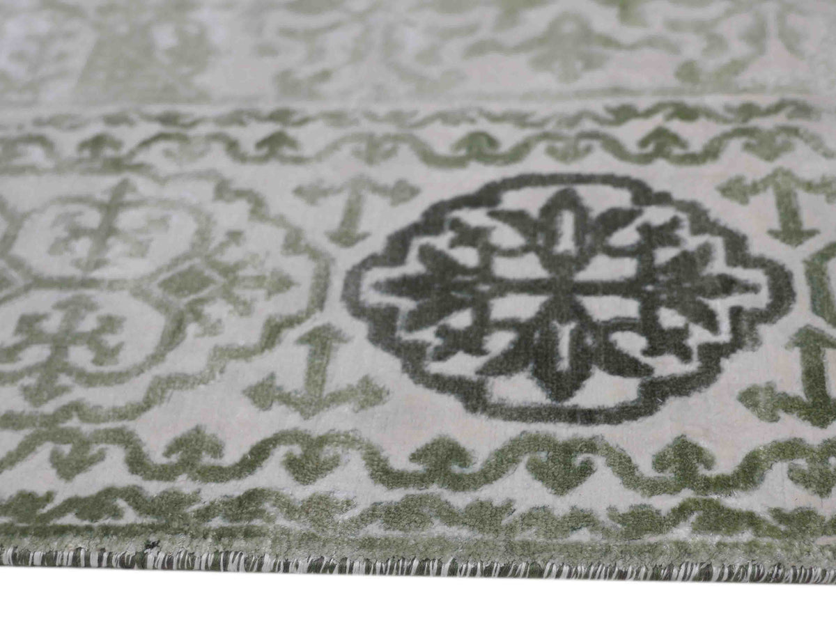 Close-up of an ornate green and white rug featuring intricate geometric patterns and floral motifs, conveying a sense of elegance and tradition.