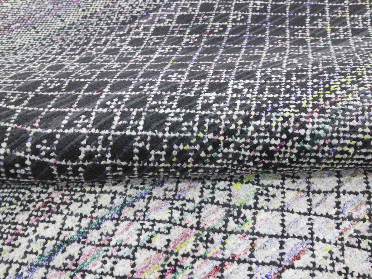 Close-up of a textured, woven fabric featuring a black and white checkerboard pattern with random splashes of colorful threads, creating a lively, artistic effect.